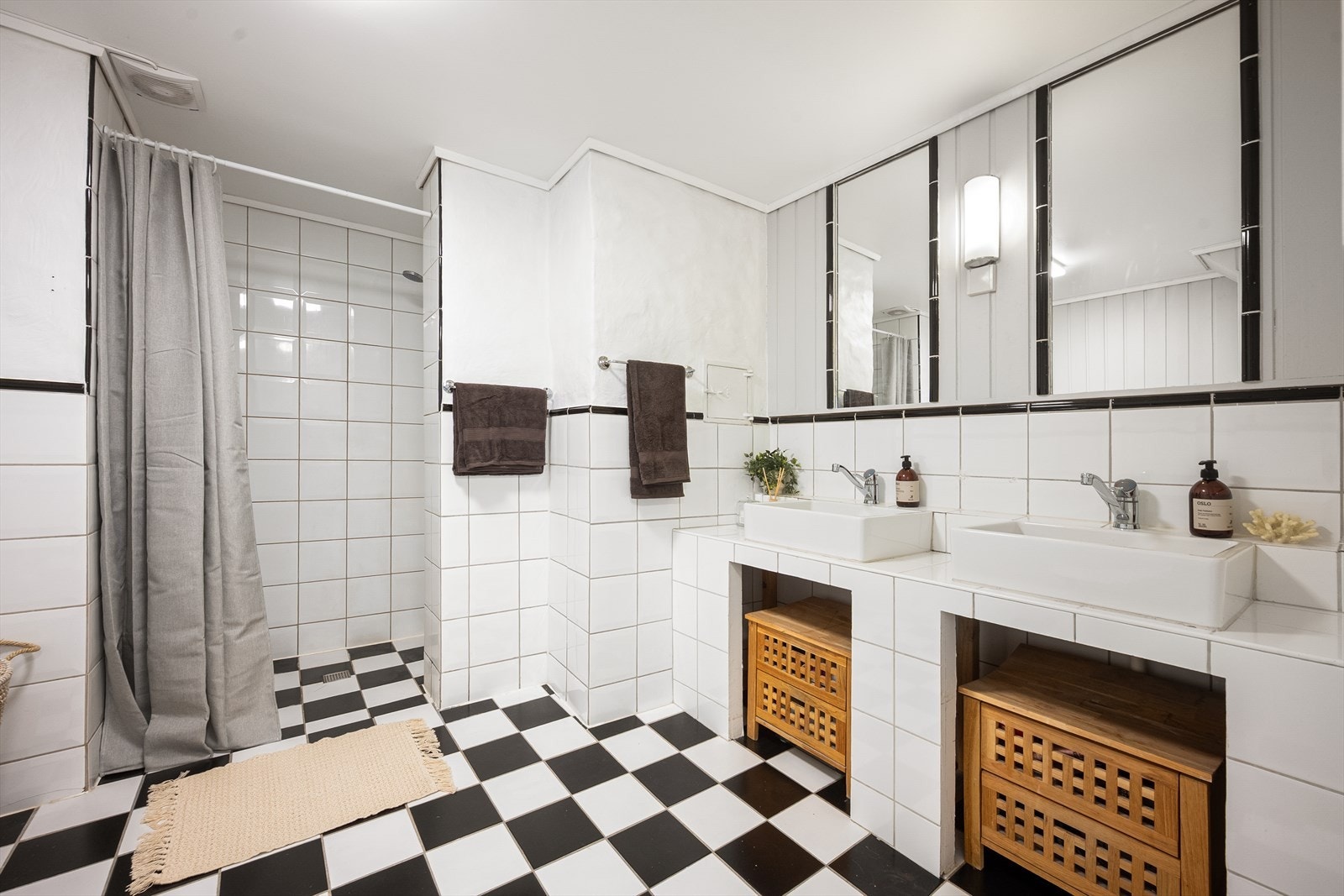 Badet er innredet med dusjsone med forheng, gulvstående toalett og bred baderomsinnredning med to servanter, vegghengte speil og belysning. Galleribilde