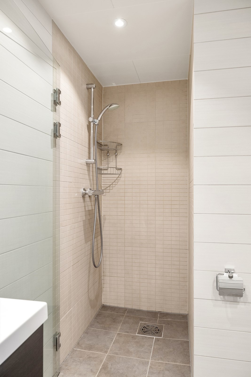 Badet har varmekabler i gulv og innredet med servant i baderomsmøbel, veggmontert toalett og dusjvegger/hjørne. Galleribilde