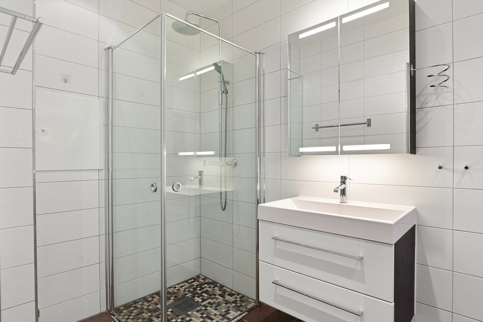 Badet er utstyrt med baderomsinnredning med nedfelt servant og speilskap med integrert belysning over. Dusjhjørne med fossefalldusj og innfellbare glassdører. Galleribilde