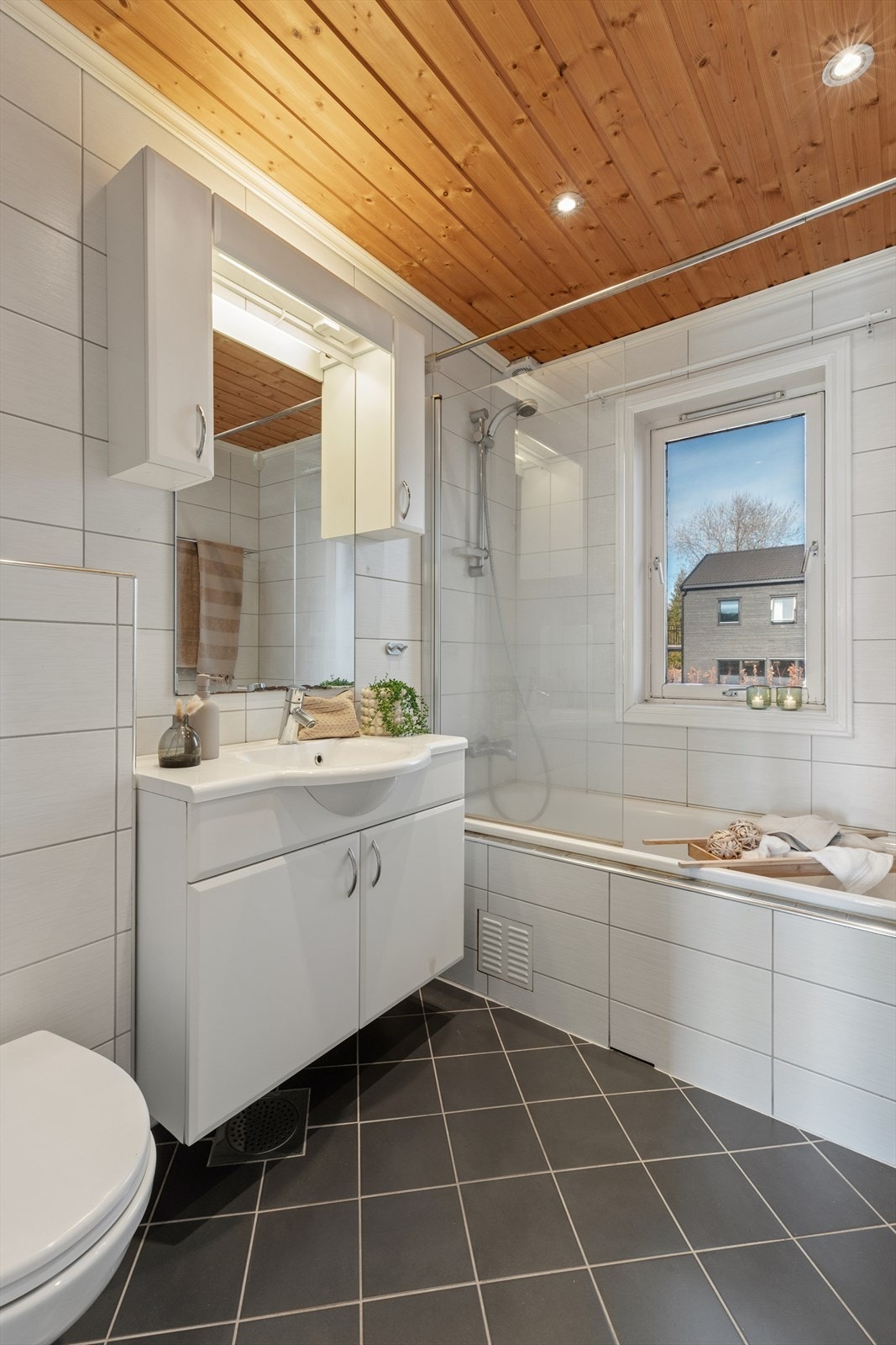 Badet er innredet med vegghengt toalett, innemurt badekar med glassvegg, samt baderomsinnrening med servant og speil med belysning. Galleribilde