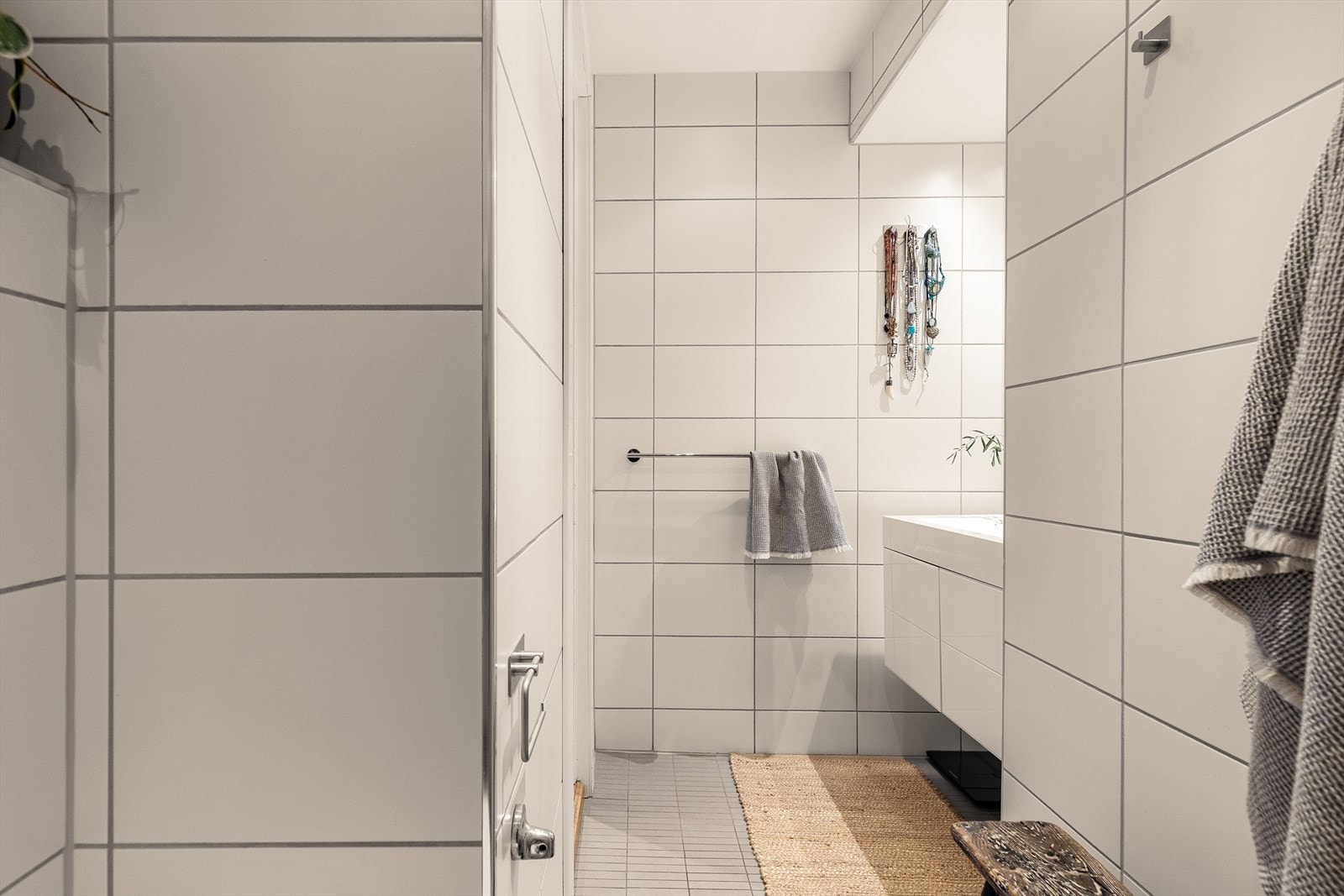 Rommet er utstyrt med veggmontert toalett, dusjhjørne med innfellbare glassdører og baderomsinnredning med skap, servant med ettgreps blandebatteri og vegghengt speilskap. Galleribilde