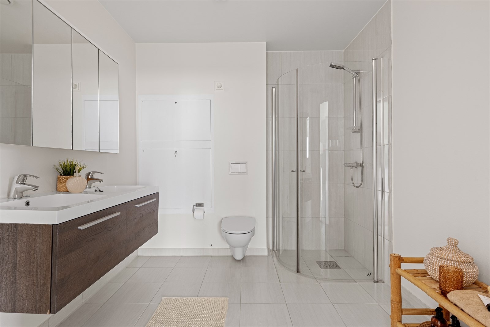 Badet har innredning med dobbel servant nedfelt i benkeskap, veggskap med speilfronter, vegghengt toalett som er lekkasjesikret med safetybag, dusjhjørne med glassdører og opplegg/plass for vaskemaskin Galleribilde