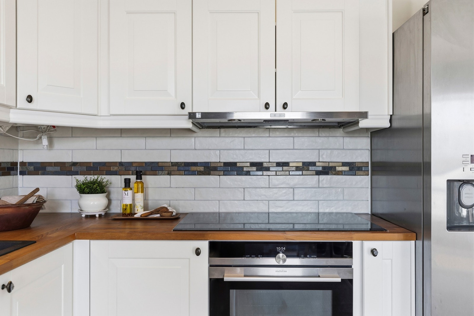 Utstyrt med integrert induksjonstopp, stor komfyr med dampfunksjon, og oppvaskmaskin, samt et praktisk side by side kjøle og fryseskap Galleribilde