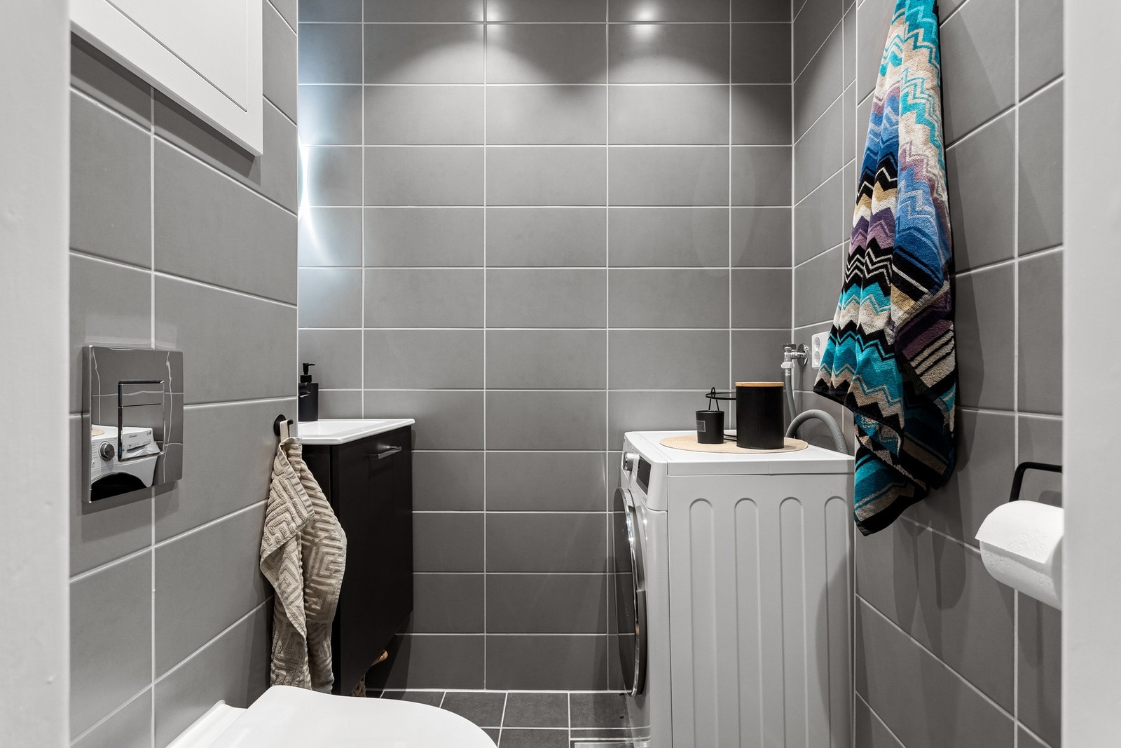 Toalettrommet er utstyrt med moderne servantskap med sort armatur, rundt speil med integrert belysning og vegghengt toalett. Galleribilde