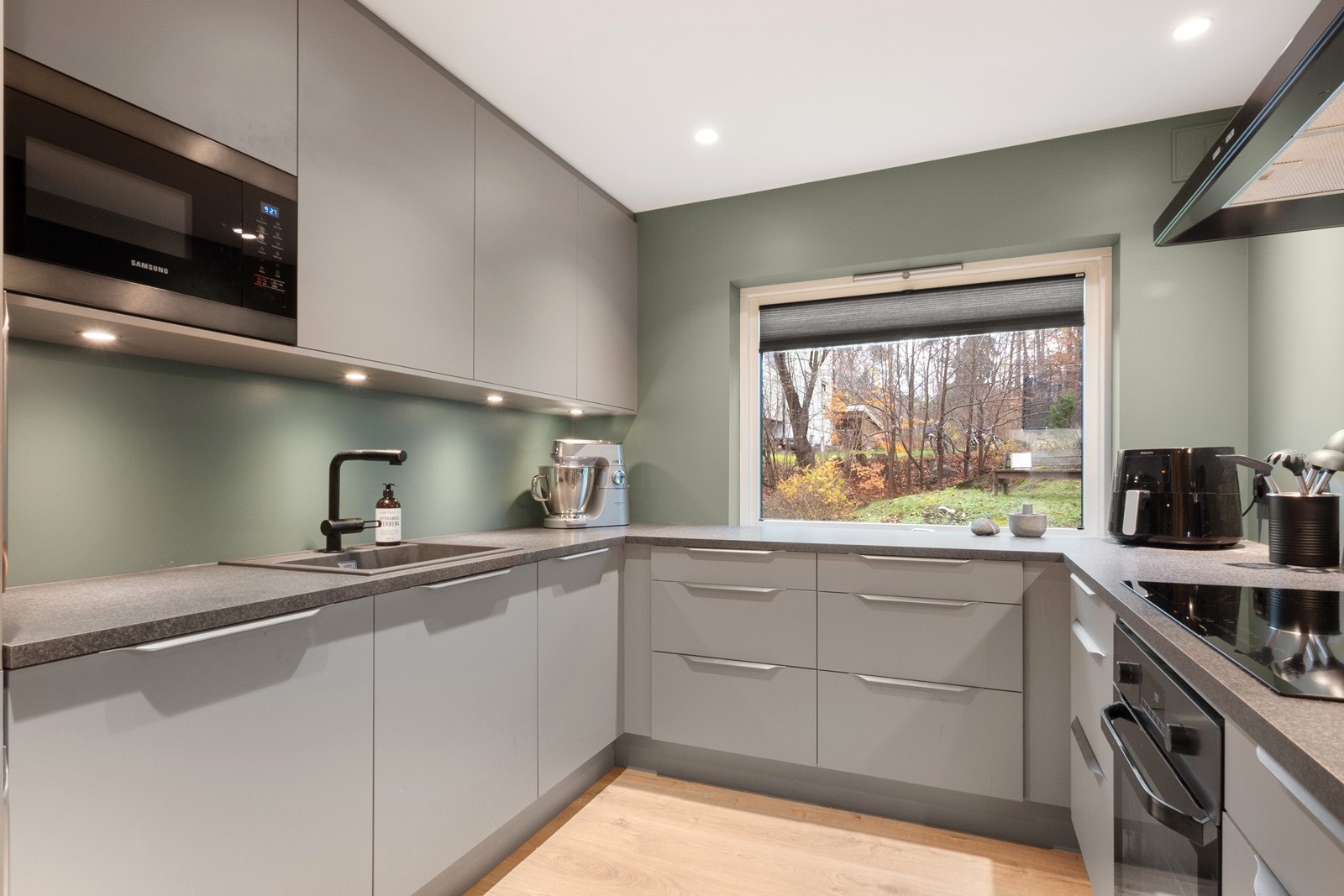 Kjøkkenet har en stilren kjøkkeninnredning fra HTH-kjøkken fra 2019 med slette fronter i lys grå, laminat benkeplate og komposittkum. Galleribilde