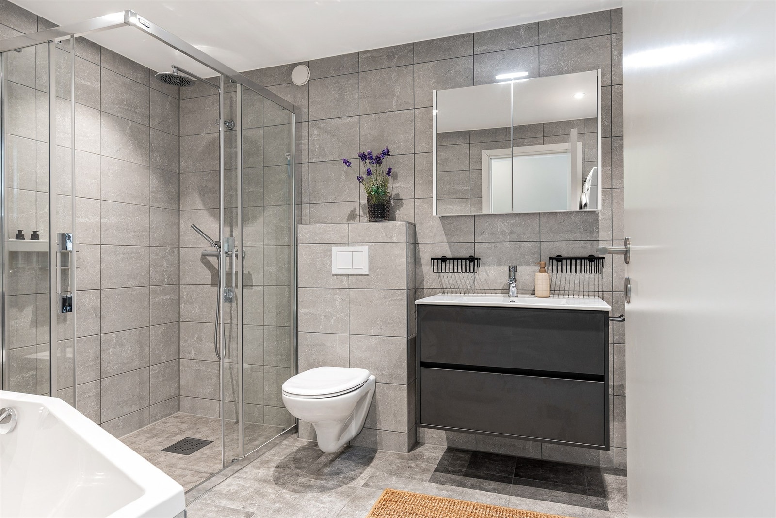 Badet har vegghengt toalett, servantinnredning med skuffer og speilskap. Det er varme i gulvet. Galleribilde