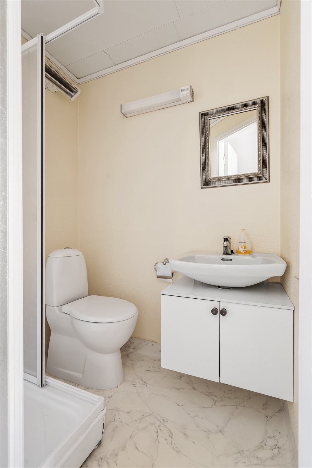 Badet har en eldre enkel standard med vinylbelegg på gulv og vegger mede tapet/belegg - Rommet er utstyrt med toalett, dusjkabinett og servantinnredning Galleribilde