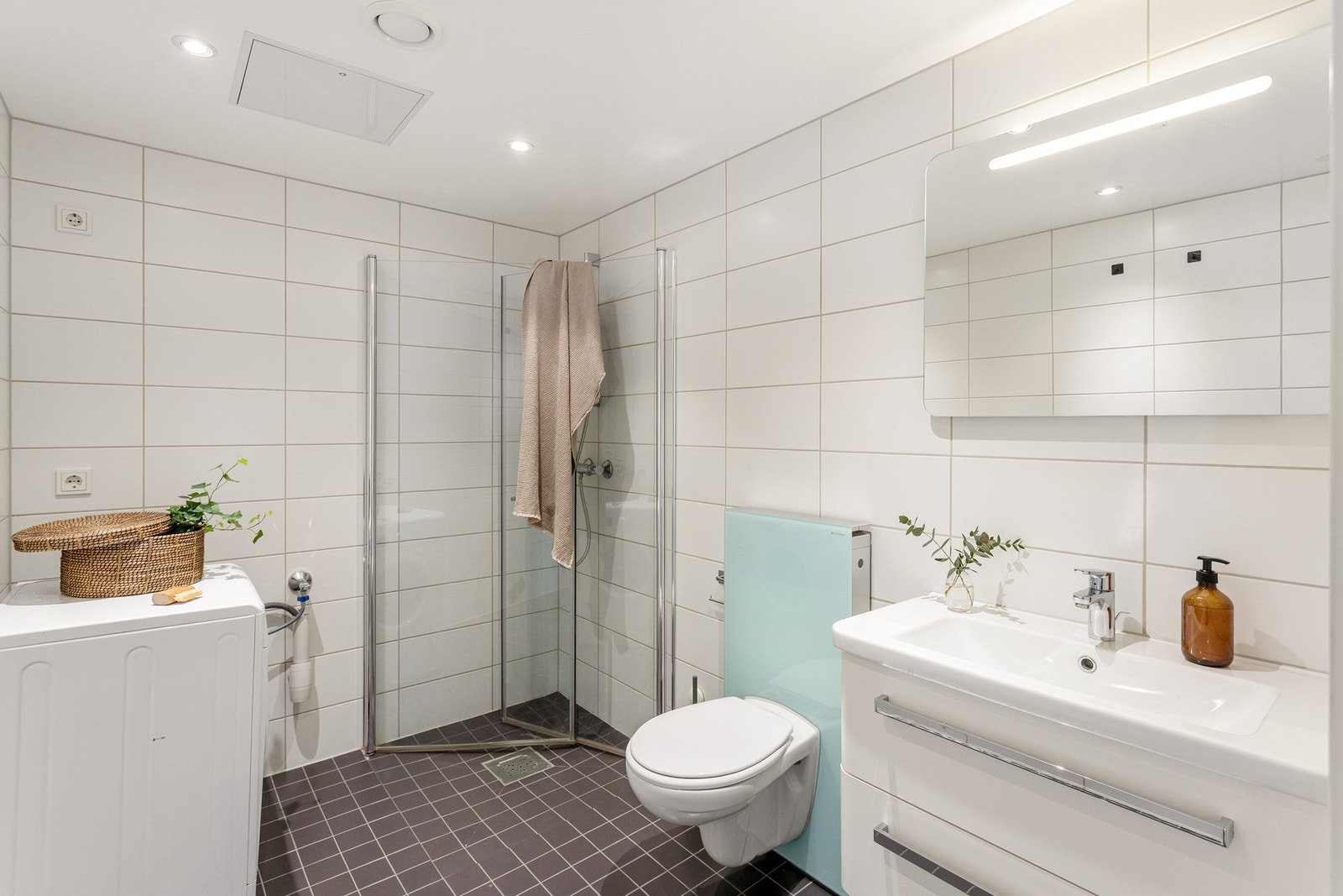 Boligen har et innbydende bad med inngang fra entréen. Badet er bygget opp med hvite fliser på vegg, mørke fliser på gulv, gulvvarme og downlights i tak med dimmer. Galleribilde