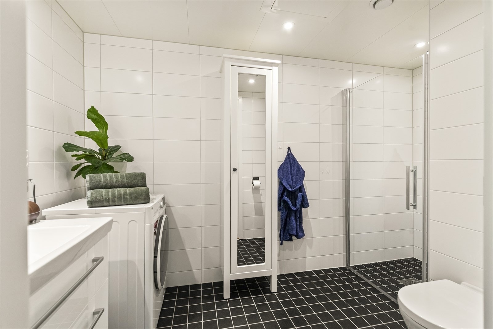 Badet er et delikat, flislagt rom. Det er stilrent med mørke fliser på gulv og lyse fliser på vegger. Galleribilde