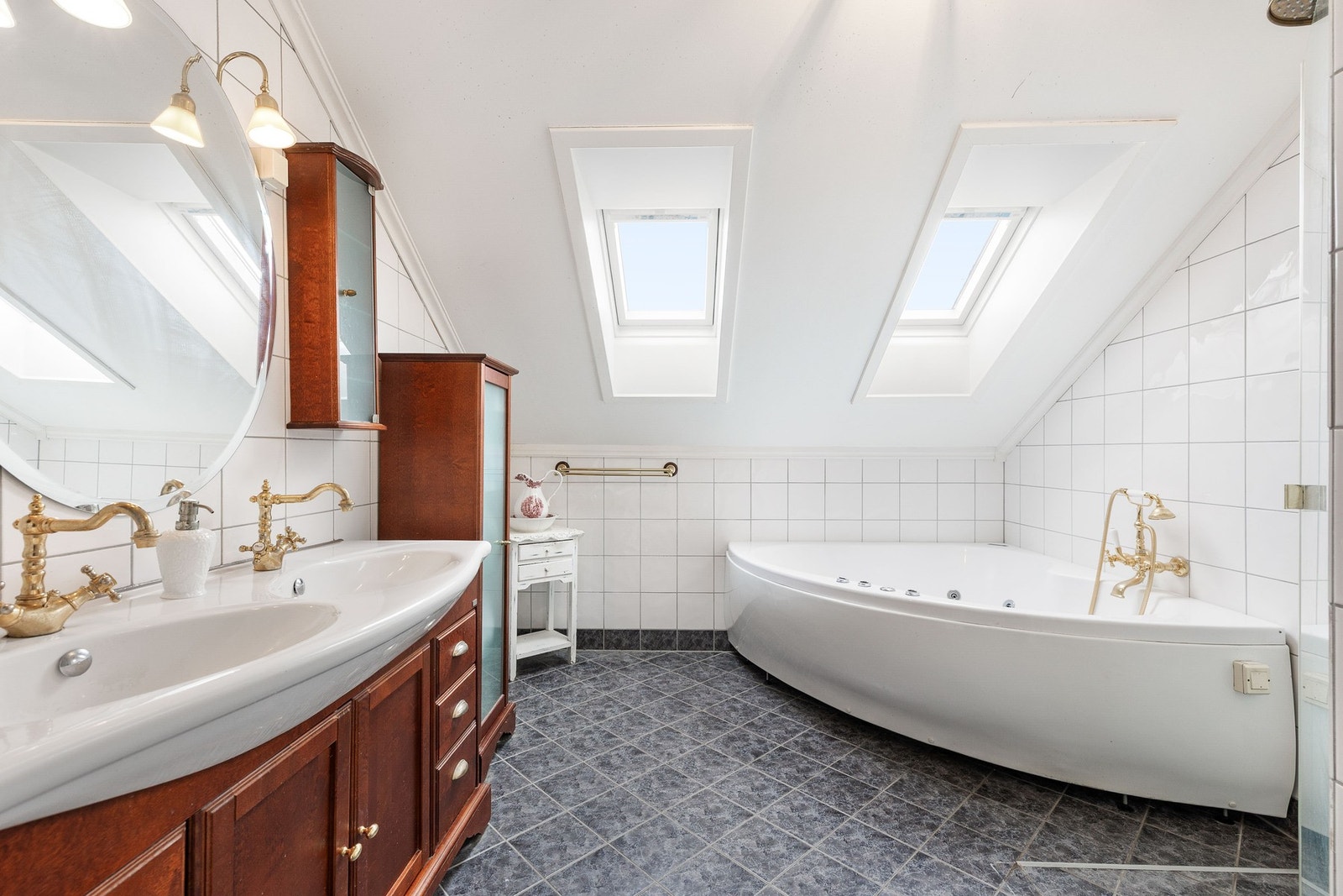 Lyst bad med skråtak, dobbelt servant og hjørnebadekar. Takvinduer gir et flott overlys i rommet. Galleribilde