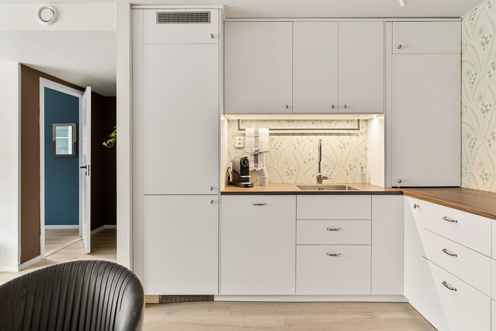 Innredningen består av moderne skap, skuffer og downlights. Den mørkere benkeplaten står i flott stil med de lyse frontene og tapet i bakgrunn gir en fin kontrast til rommet. Galleribilde