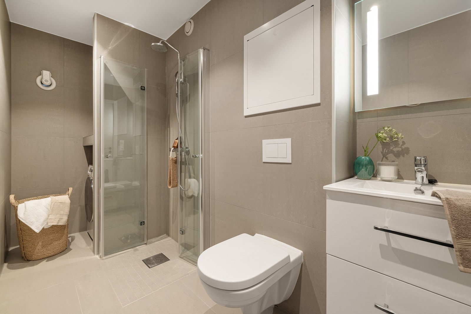 Rommet inneholder innredning med servant, vegghengt toalett, dusjhjørne og opplegg for vaskemaskin Galleribilde