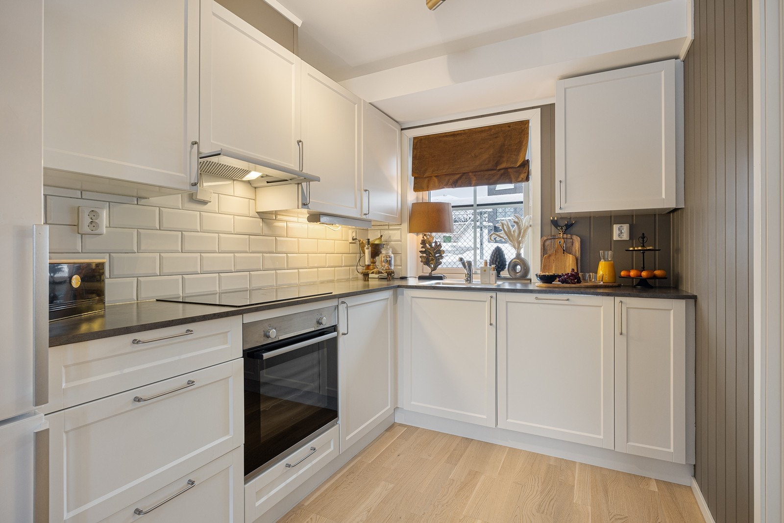 Over benken er det belysning og hvite metrofliser, og over kokesonen har kjøkkenet en komfyrvakt og en ventilator. Galleribilde