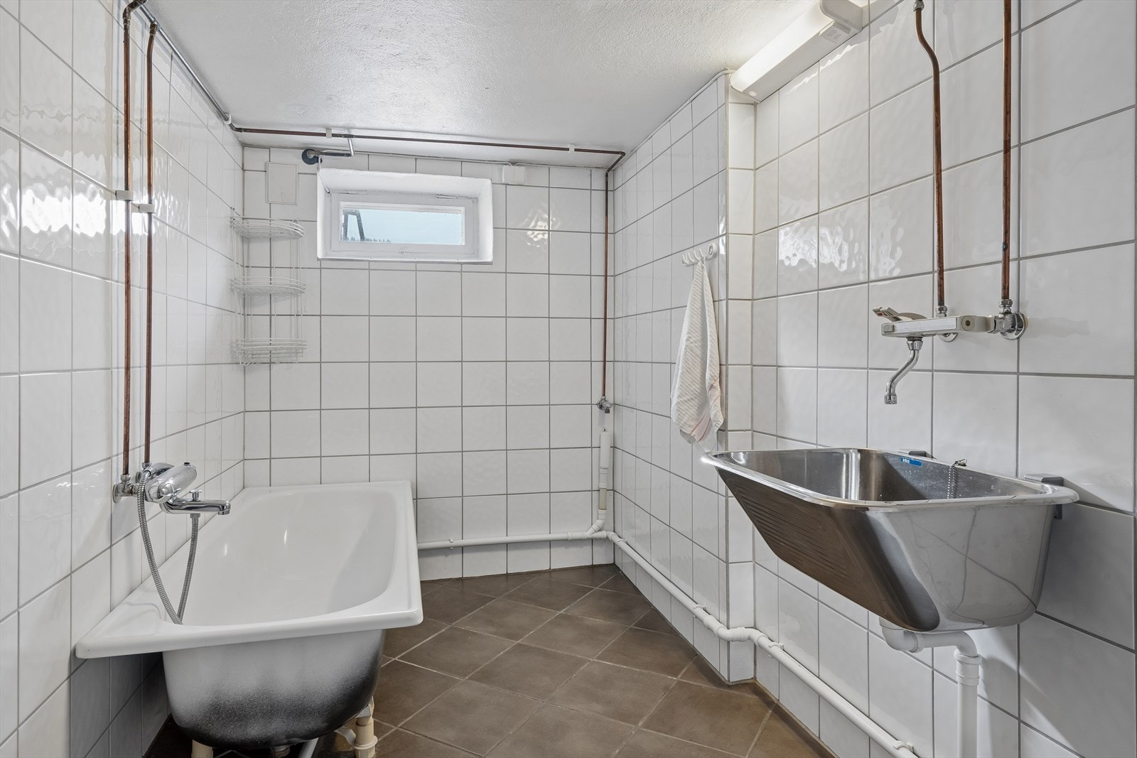 Praktisk vaskerom i kjelleren med flislagt gulv med varmekabler, badekar og opplegg for vaskemaskin. Galleribilde