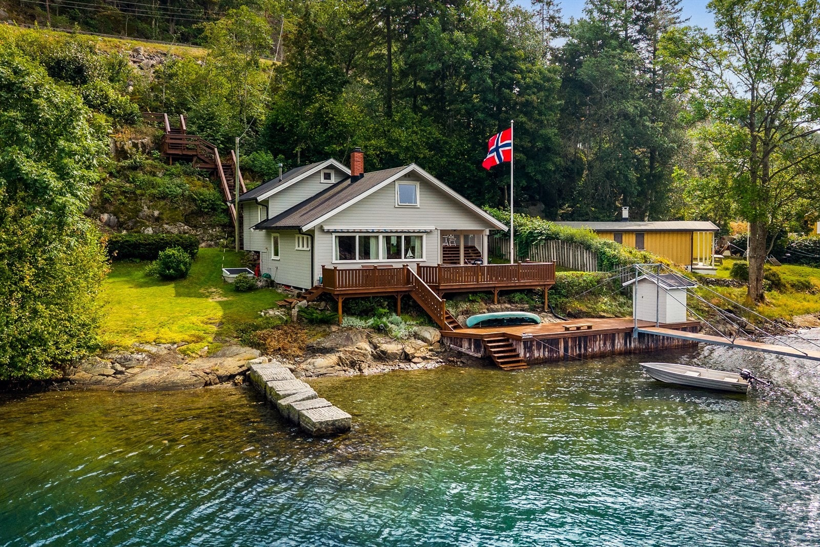 Et overblikk over hele strandlinjen, med hytta lunt plassert i det grønne. Galleribilde