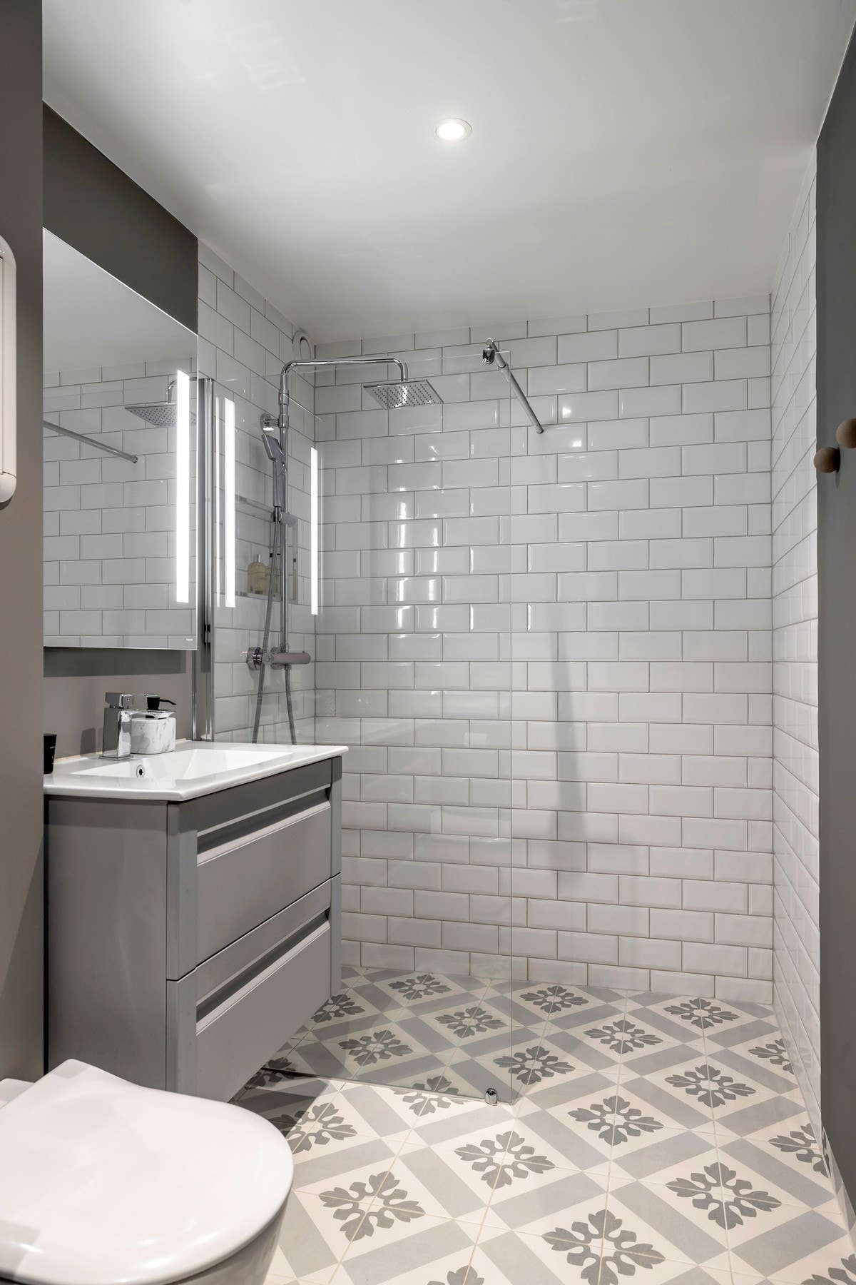 Badet er flislagt og fremstår som moderne og funksjonelt. Rommet er innredet med dusjsone, vegghengt toalett og servant med tilhørende innredning. Galleribilde