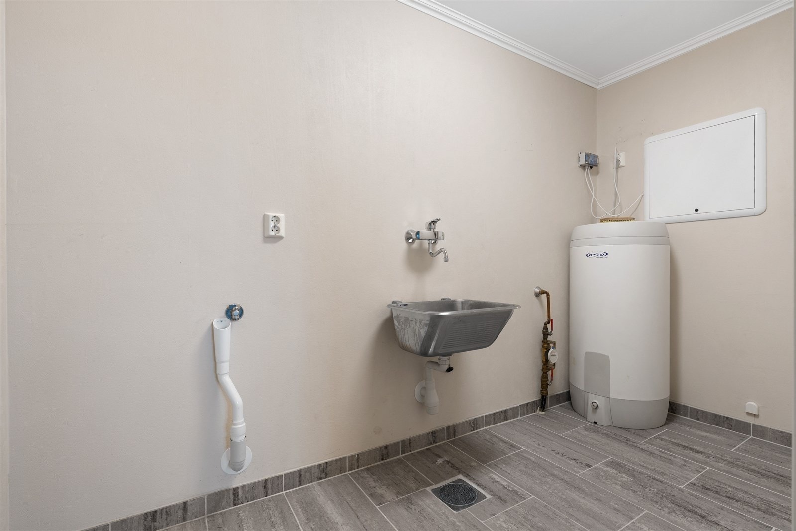 Praktisk vaskerom med flislagt gulv, utslagsvask og opplegg for vaskemaskin og tørketrommel. Galleribilde