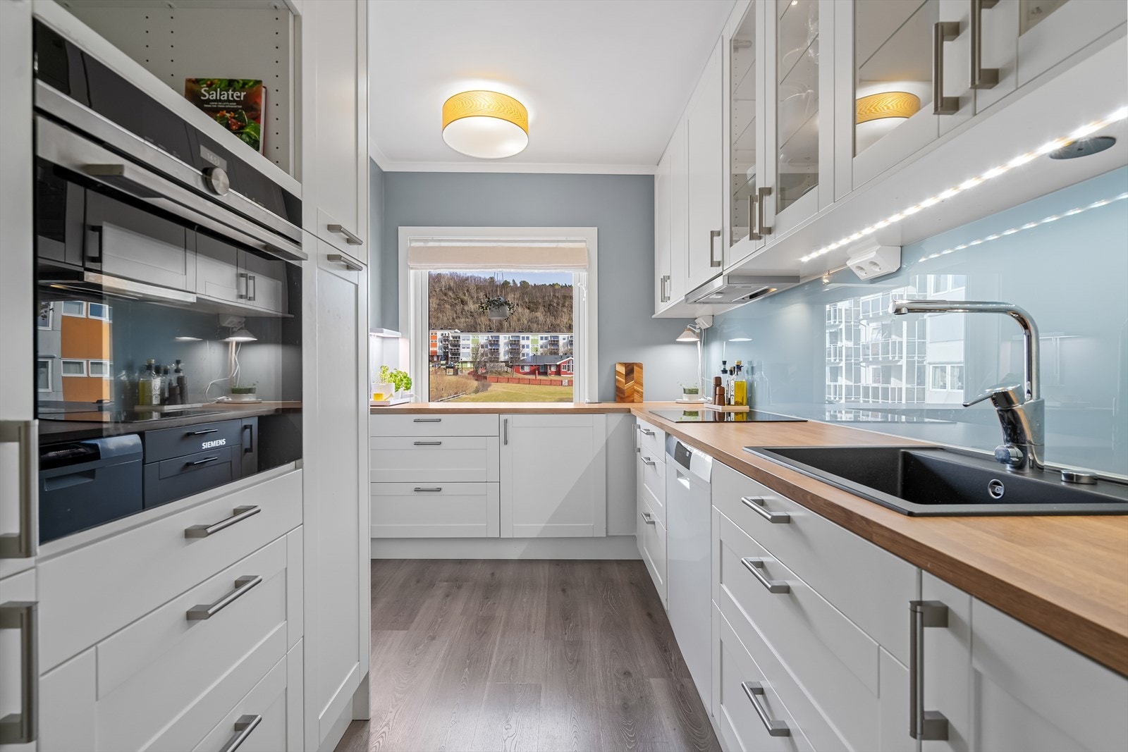 Kjøkkeninnredningen og hvitevarene er fra 2021 - Innredningen er stilren med profilerte hvite fronter, benkeplate i laminat og glassplate på vegg over benk. Klargjort plass til integrert micro/kaffemaskin. Galleribilde