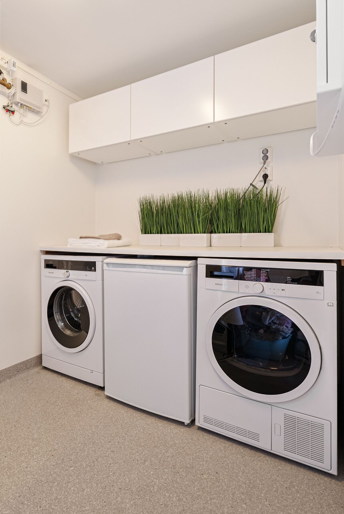 Vaskerom/teknisk rom praktisk innredet med benkeplate, skapinnredning og opplegg for vaskemaskin og tørketrommel. Galleribilde