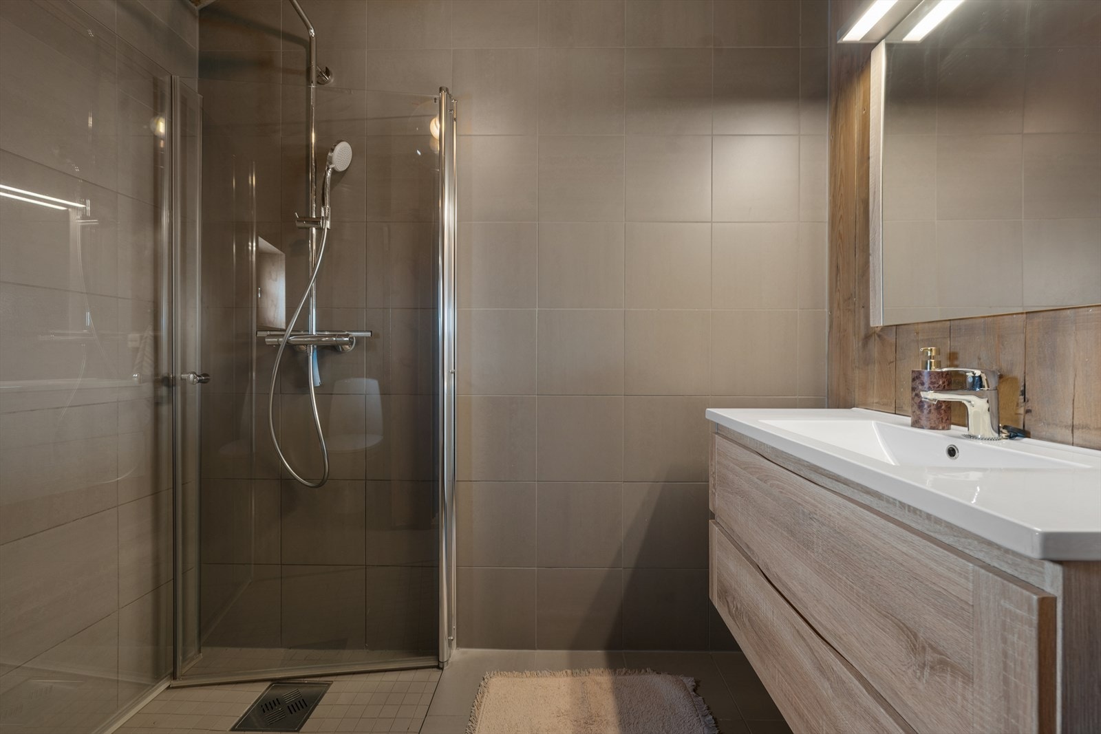 Badet har praktisk dusjløsning, og fliser på gulv og vegger Galleribilde
