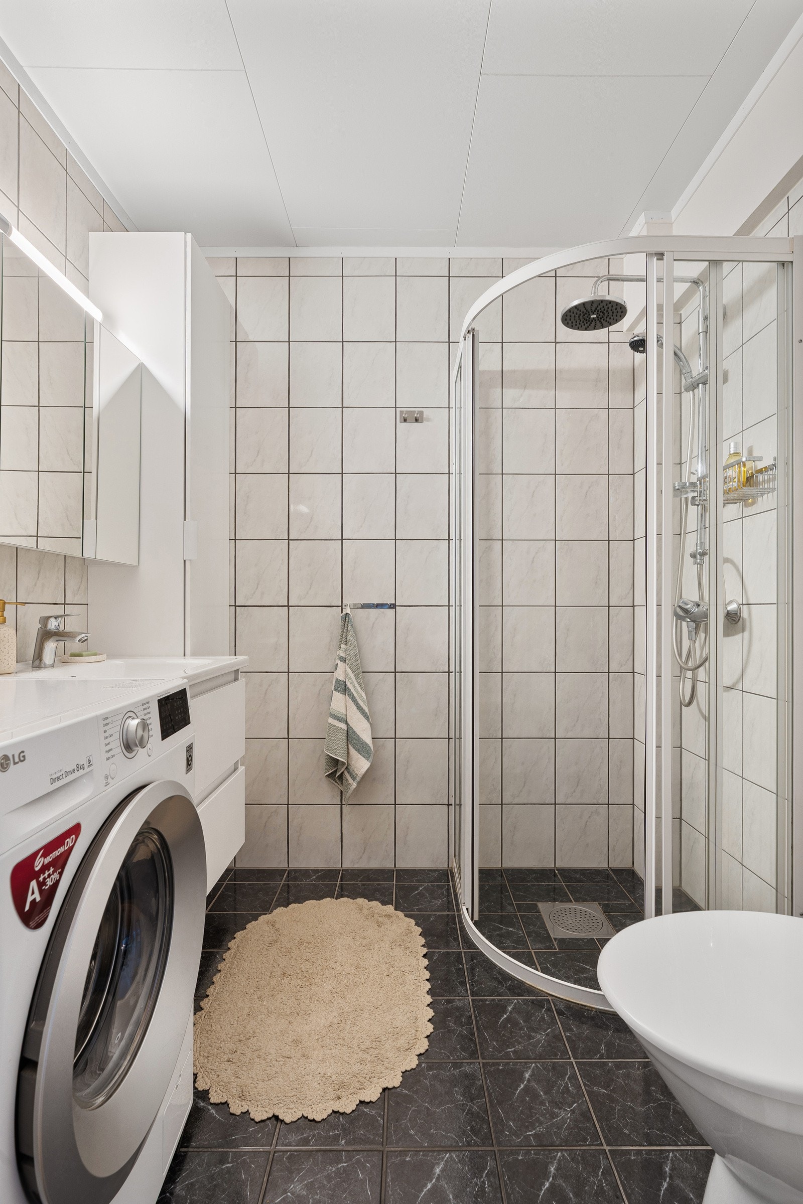 Flislagt bad med dusjhjørne, innredning med speilskap og plass til vaskemaskin. Galleribilde