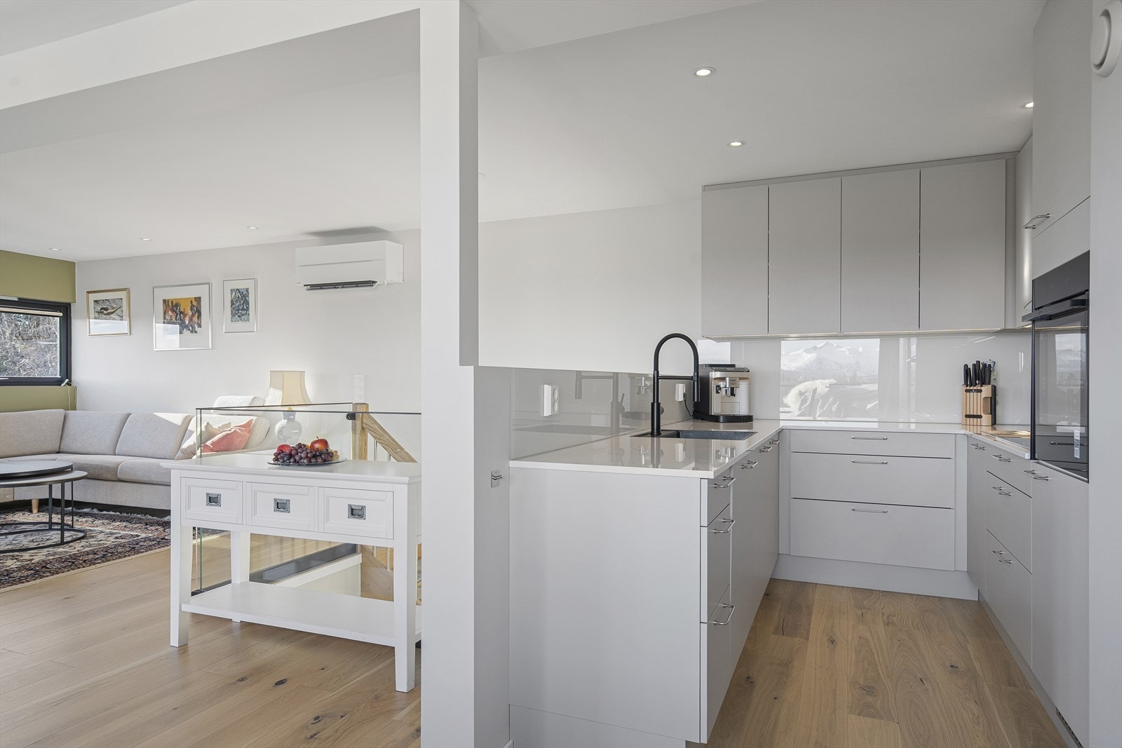 Stilrent kjøkken fra Designa med innredning med glatte fronter, benkeplate i stein og glassplater på vegg over benk Galleribilde