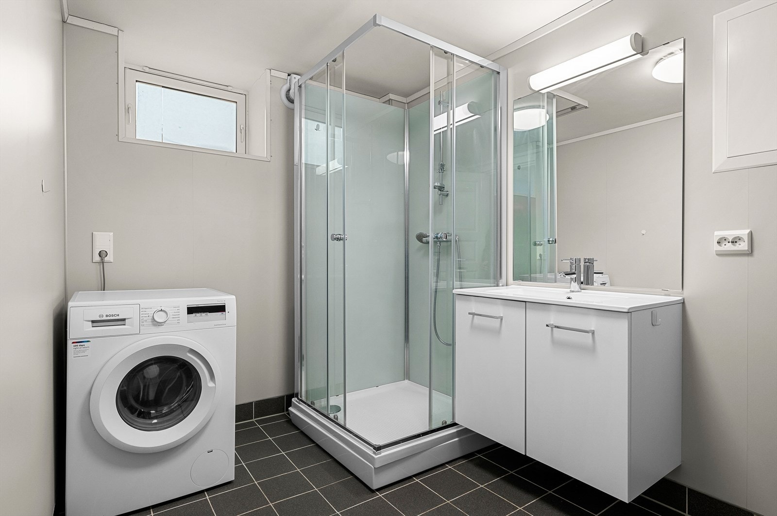 Badet har flislagt gulv med gulvvarme. Det er innredet med dusjkabinett, opplegg for vaskemaskin, servant og servantskap. Galleribilde