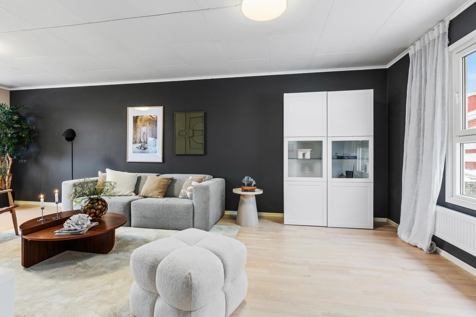 Stue med lyst gulv, mørke vegger og store vinduer som gir godt med naturlig lys. Galleribilde