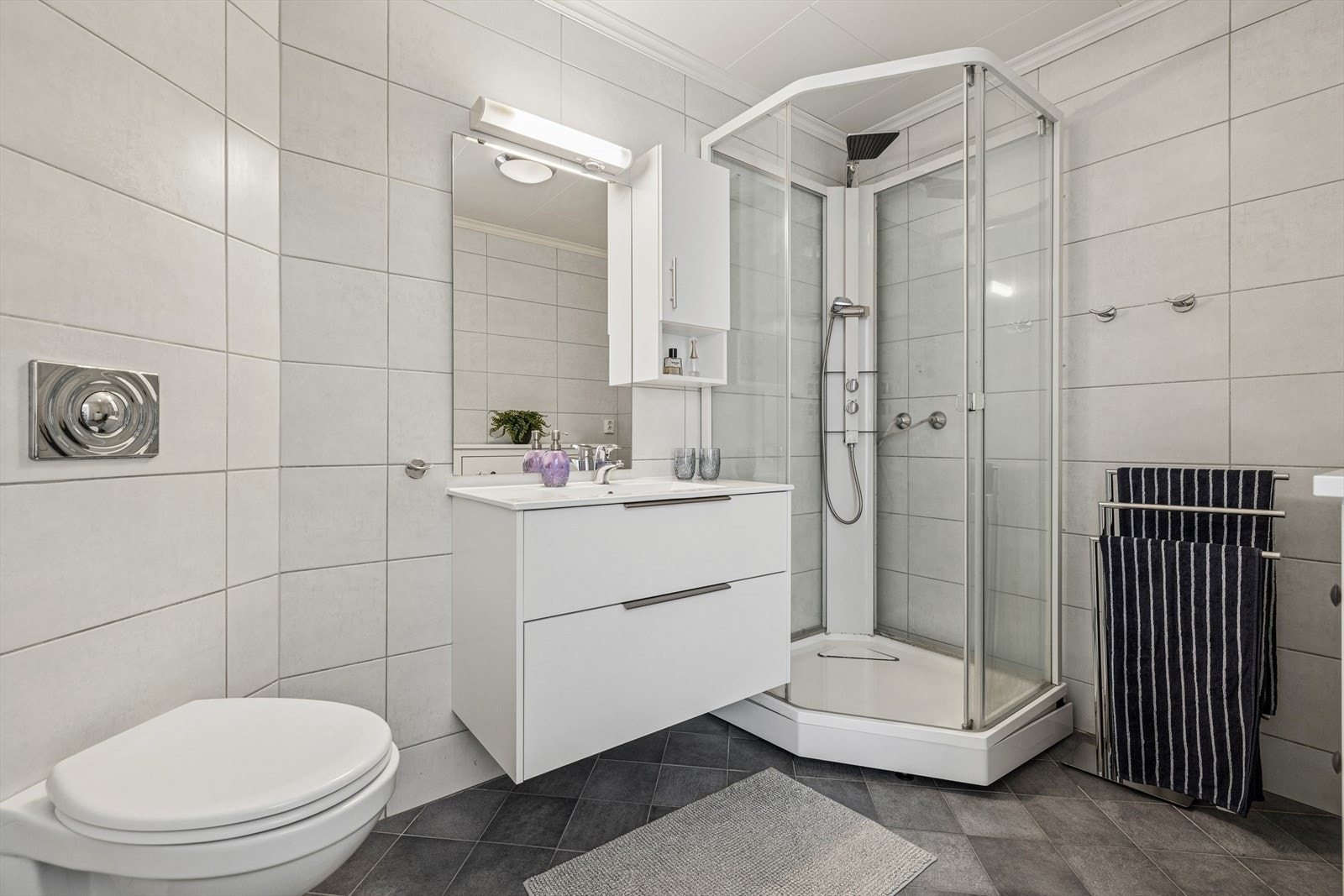 I boligens første etasje finner vi et tidløst, pent og innbydende baderom. Badet er gjennomført med pene fliser på gulv og vegger. Galleribilde