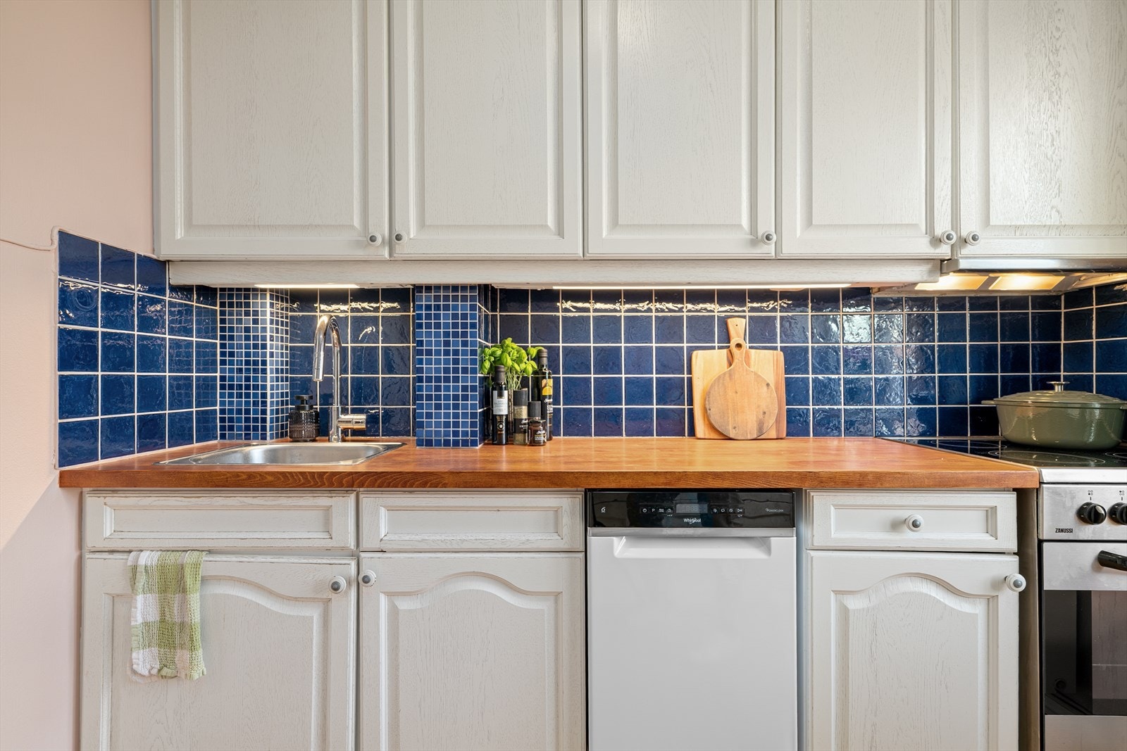 Benkeplaten i tre har en nedfelt kum i rustfritt stål, og det er fliser på veggen over benken. Galleribilde