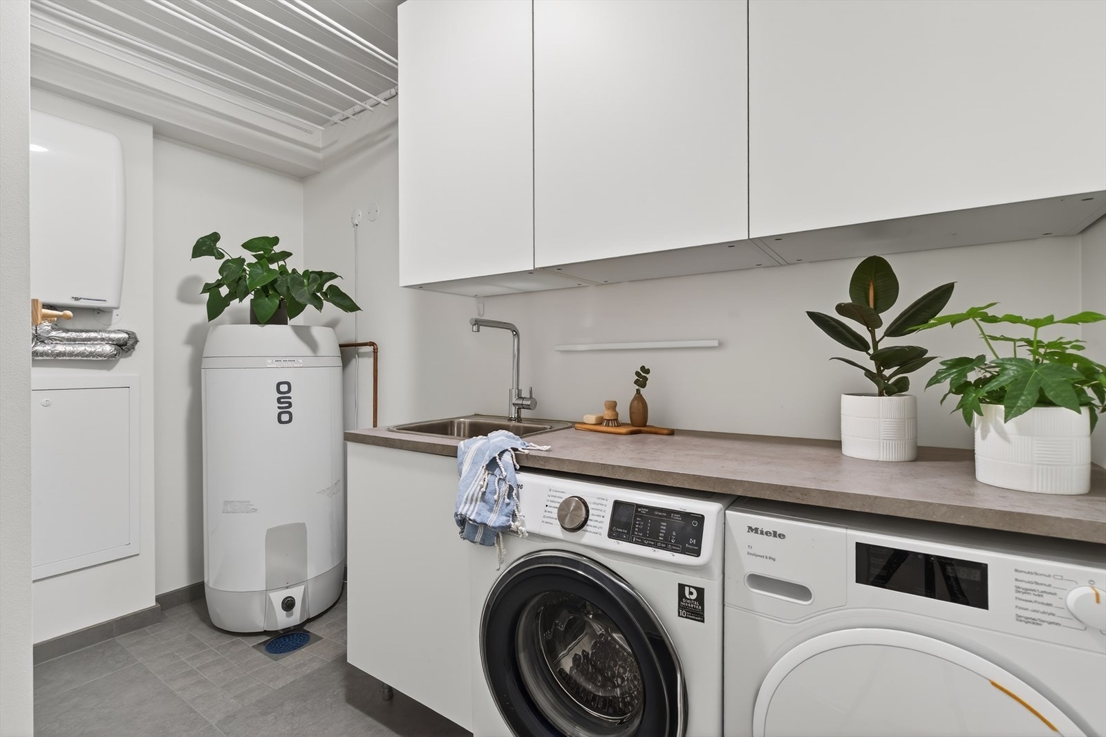 Vaskerom har innredning med nedfelt servant og opplegg for vaskemaskin. Det er balansert ventilasjon. Gulvet er flislagt og det er montert vannbåren gulvvarme. Veggene har malte plater. Taket er malt. Galleribilde