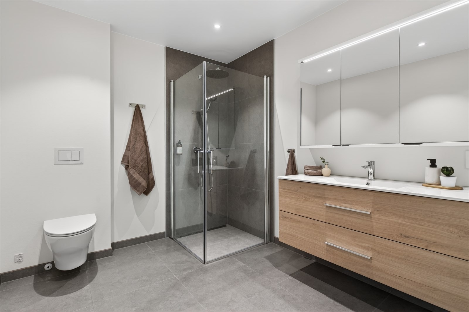 Stilrent baderom, innredning med heldekkende servant, veggmontert toalett og dusjvegger/hjørne. Gulvet er flislagt og det er montert vannbåren gulvvarme. Veggene har malte plater og fliser i dusjsone. Taket er malt. Galleribilde