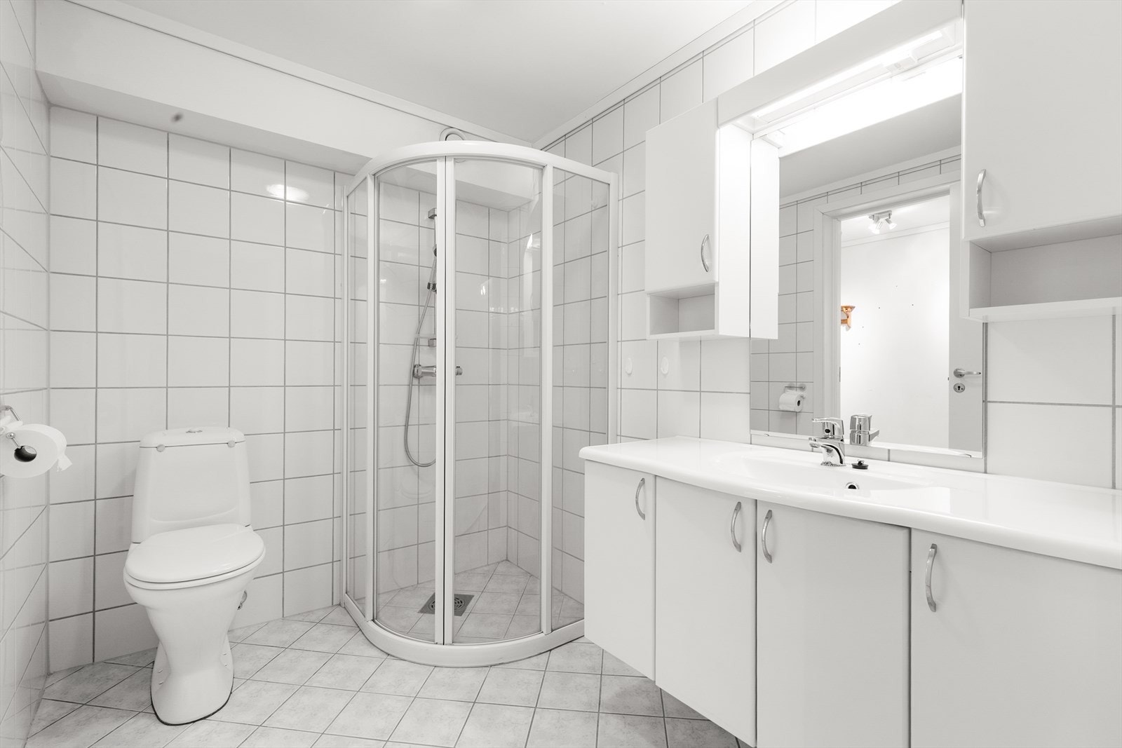 Her er det innredning med god oppbevaringsplass, heldekkende servant og speil med overlys og el-stikk. Badet er også innredet med dusjhjørne med glassvegger og toalett. Galleribilde