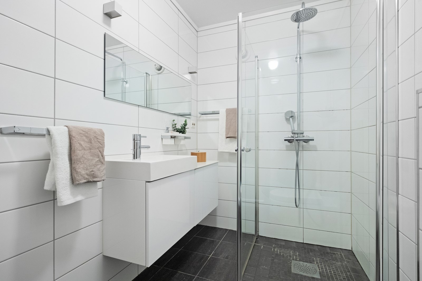 Badet er utstyrt med nedfelt servant, veggmontert toalett, dusjvegger i glass og opplegg for vaskemaskin Galleribilde