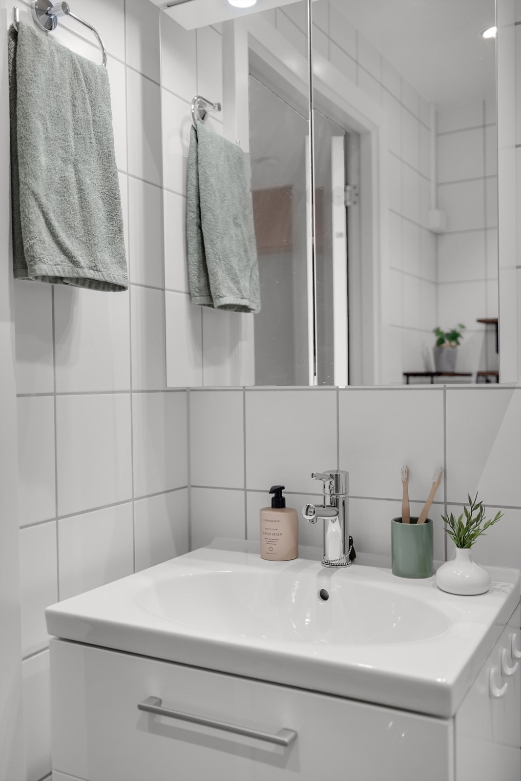 Badet er innredet med vegghengt servant med ett-greps armatur og skuffer, dusjhjørne med buet innfellbare glassdører, dusjarmatur tilkoblet veggmontert hånddusj og regndusj samt gulvstående toalett. Galleribilde