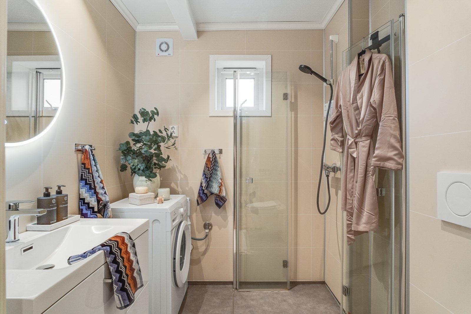 Badet inneholder vegghengt toalett, dusj og servant med baderomsinnredning, samt speil med belysning. Galleribilde