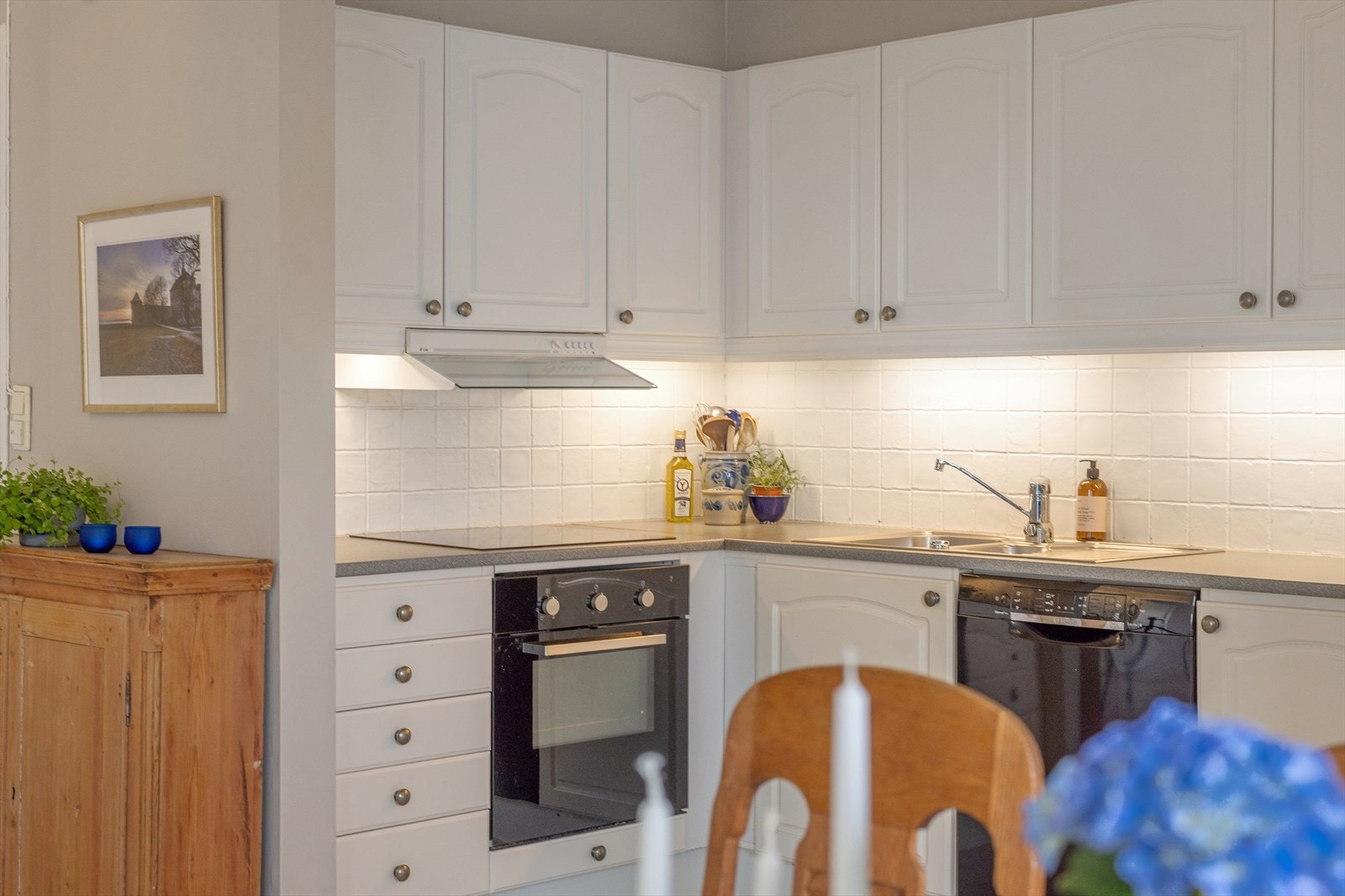 Kjøkkenet har fliser på vegg over benkeskap og belysning under overskap for en funksjonell arbeidssone. Galleribilde