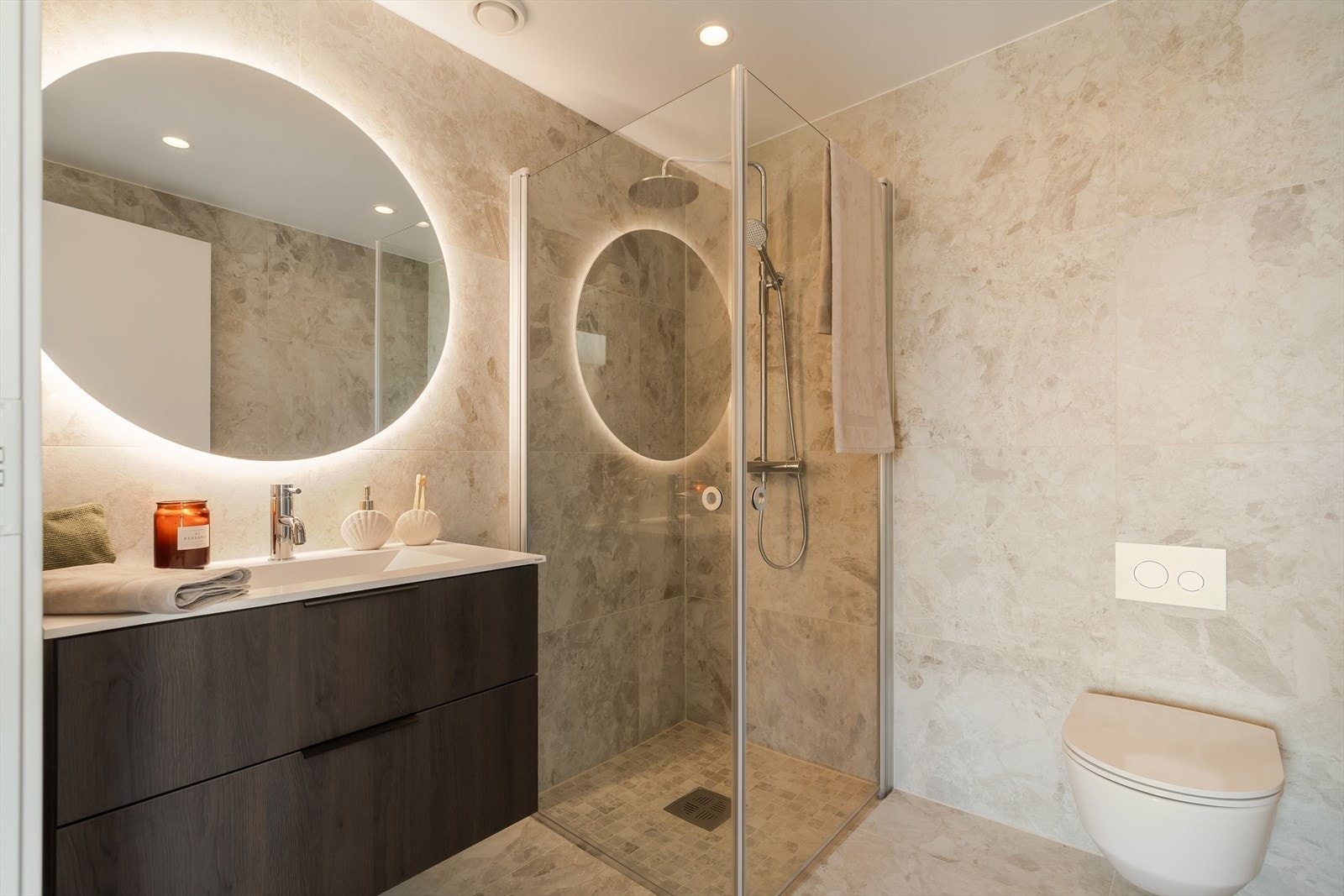 Badet fremstår stilrent og moderne med lekre flislagte overflater i lune toner. Med direkte adkomst fra hovedsoverommet får man en hotellinspirert løsning som gir både komfort og en eksklusiv følelse. Galleribilde