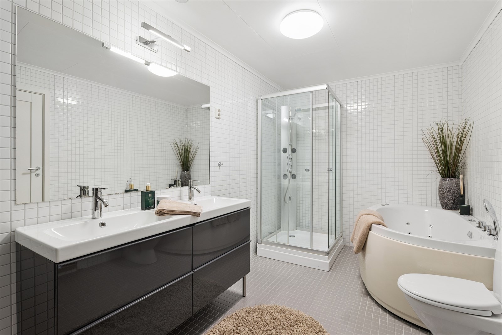 Baderom med flislagte vegger og gulv gir badet et rent og moderne uttrykk, med både dusjkabinett og badekar som gir fleksible bademuligheter. Galleribilde