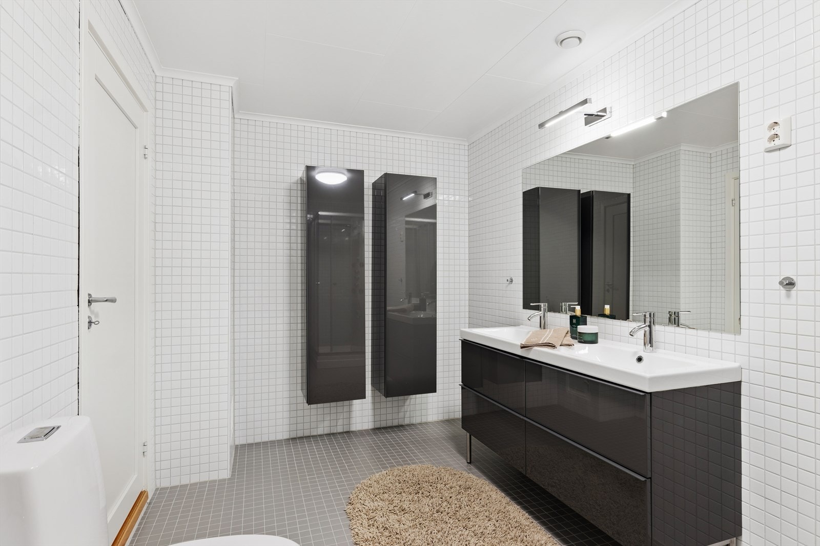 Dobbel servant med nedfelte vasker gir praktisk plass til daglig bruk, mens vegghengte skap tilbyr god oppbevaringsplass. Galleribilde