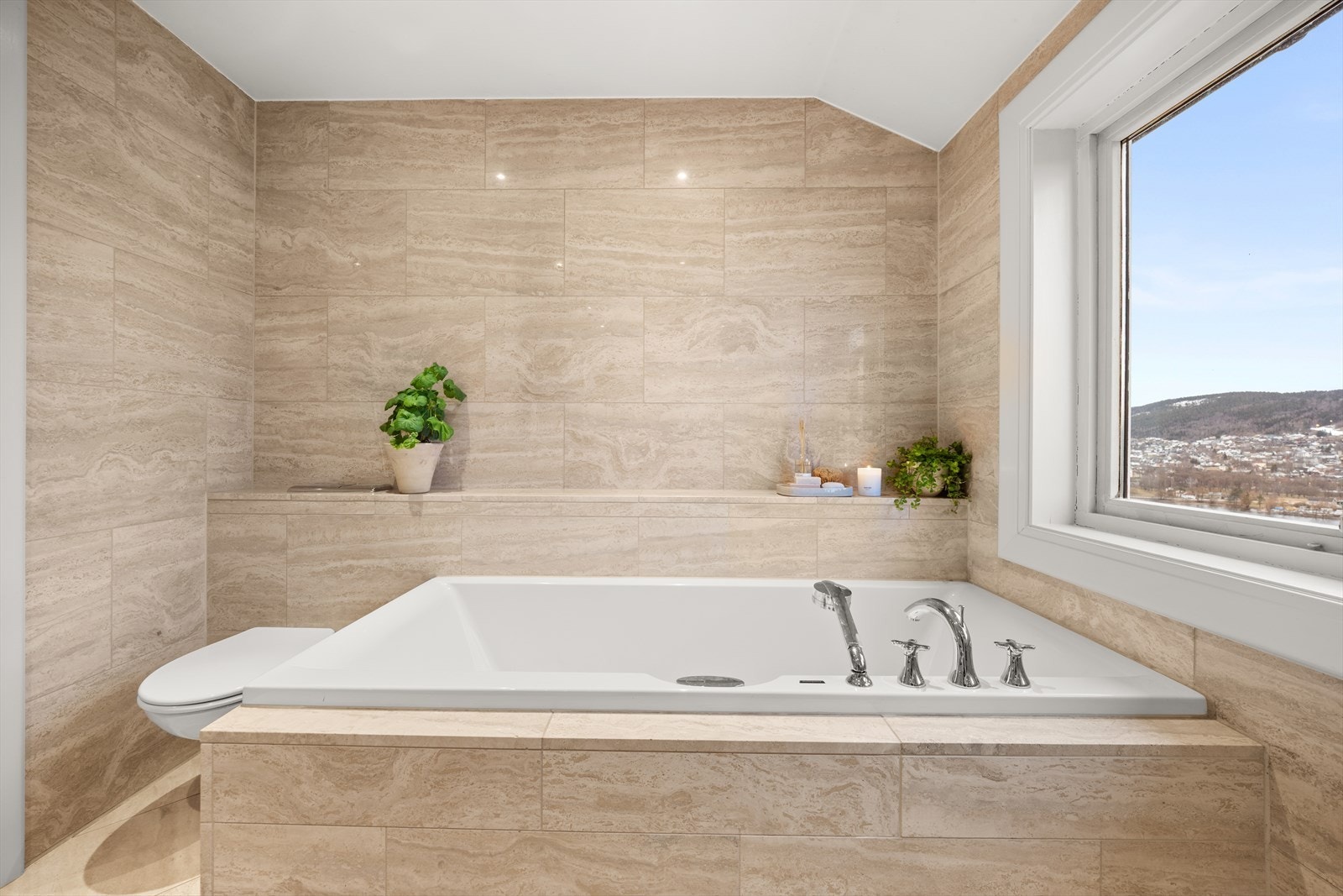 Badet er utstyrt med lekker innredning i samme fliser og med nedfelt servant, innebygd speil med innfelt belysning, dusjkabinett, vegghengt toalett og innebygd badekar Galleribilde