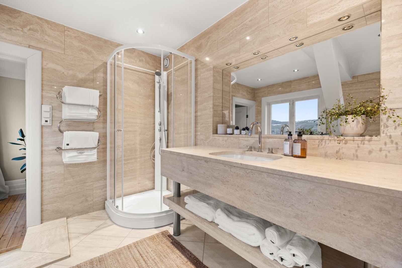 Badet er romslig og delikat med flislagte overflater i travertin og med varmekabler i gulv Galleribilde