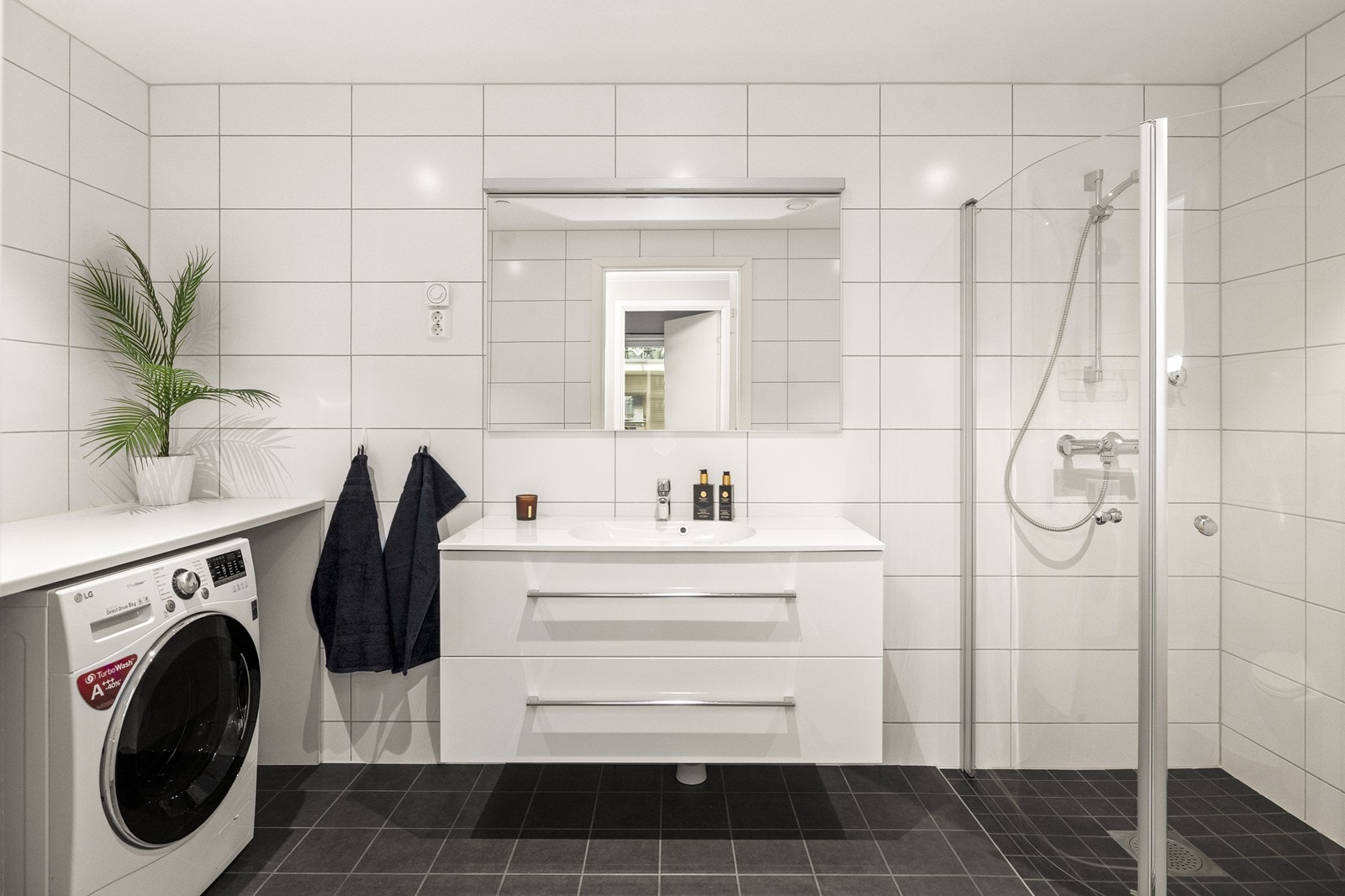 Innredningen består av en bred servant med skuffer, speil med belysning og et dusjhjørne med innfellbare glassdører. Galleribilde