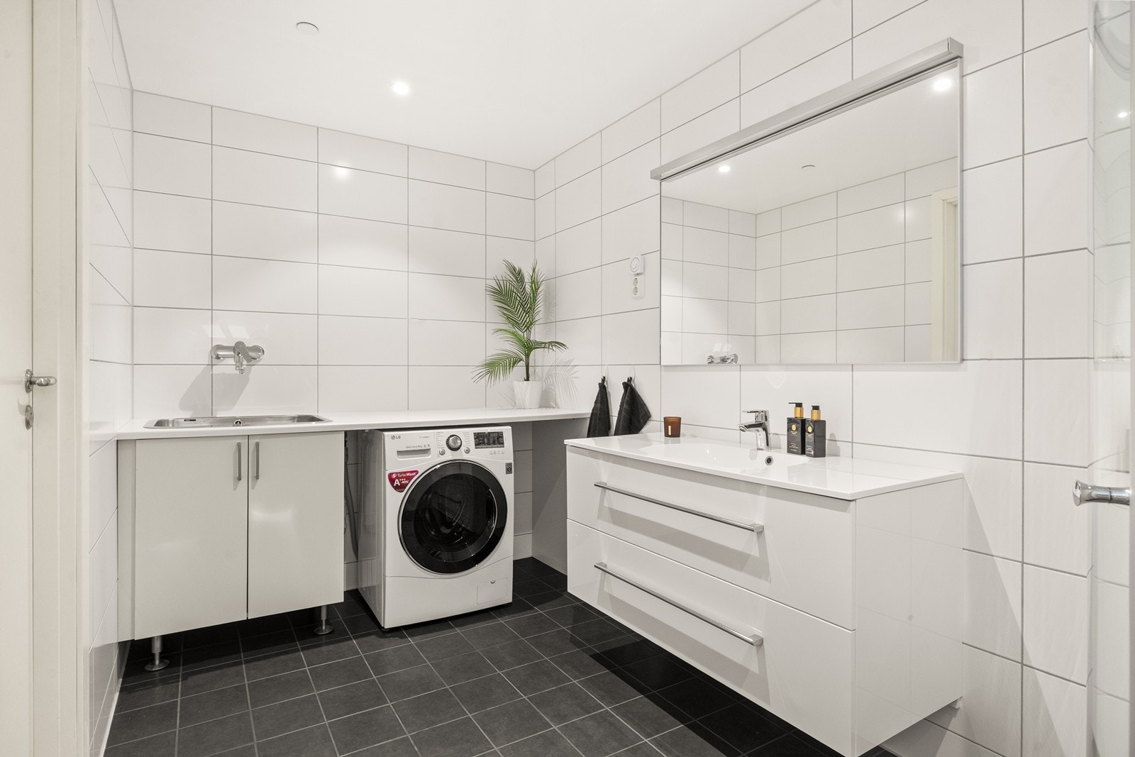 Stort, helfliset bad med vannbåren gulvvarme. Her er det en egen praktisk vaskesone med utslagsvask og opplegg for vaskemaskin. Galleribilde