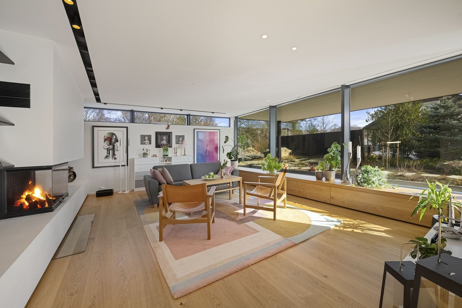 Flott dagligstue med ildsted, stedbygd benk mot store vindusfasader. Galleribilde