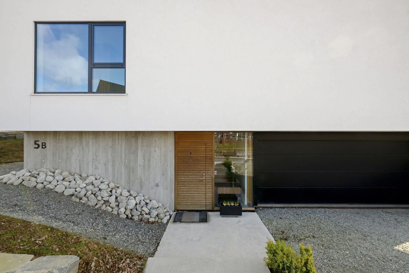 Betong, glass, pusset fasade. Brutt av heltre eikedør samt trekledning på øverste del av huset. Galleribilde