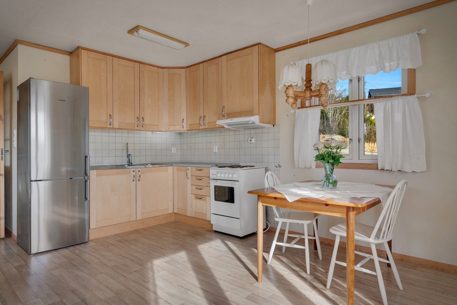 Stilrent kjøkken med profilerte fronter og laminat benkeplate, som er innredet med komfyr, ventilator og kjøl-/fryseskap. Galleribilde