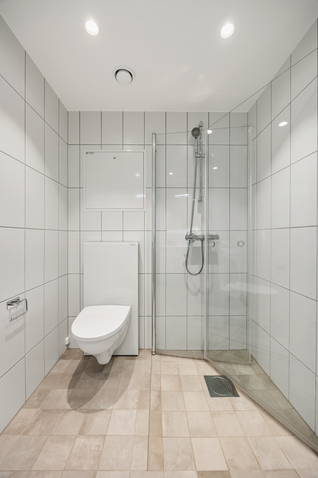 Delikat, flislagt bad med vegghengt toalett og dusjhjørne med innfellbare glassdører. Galleribilde