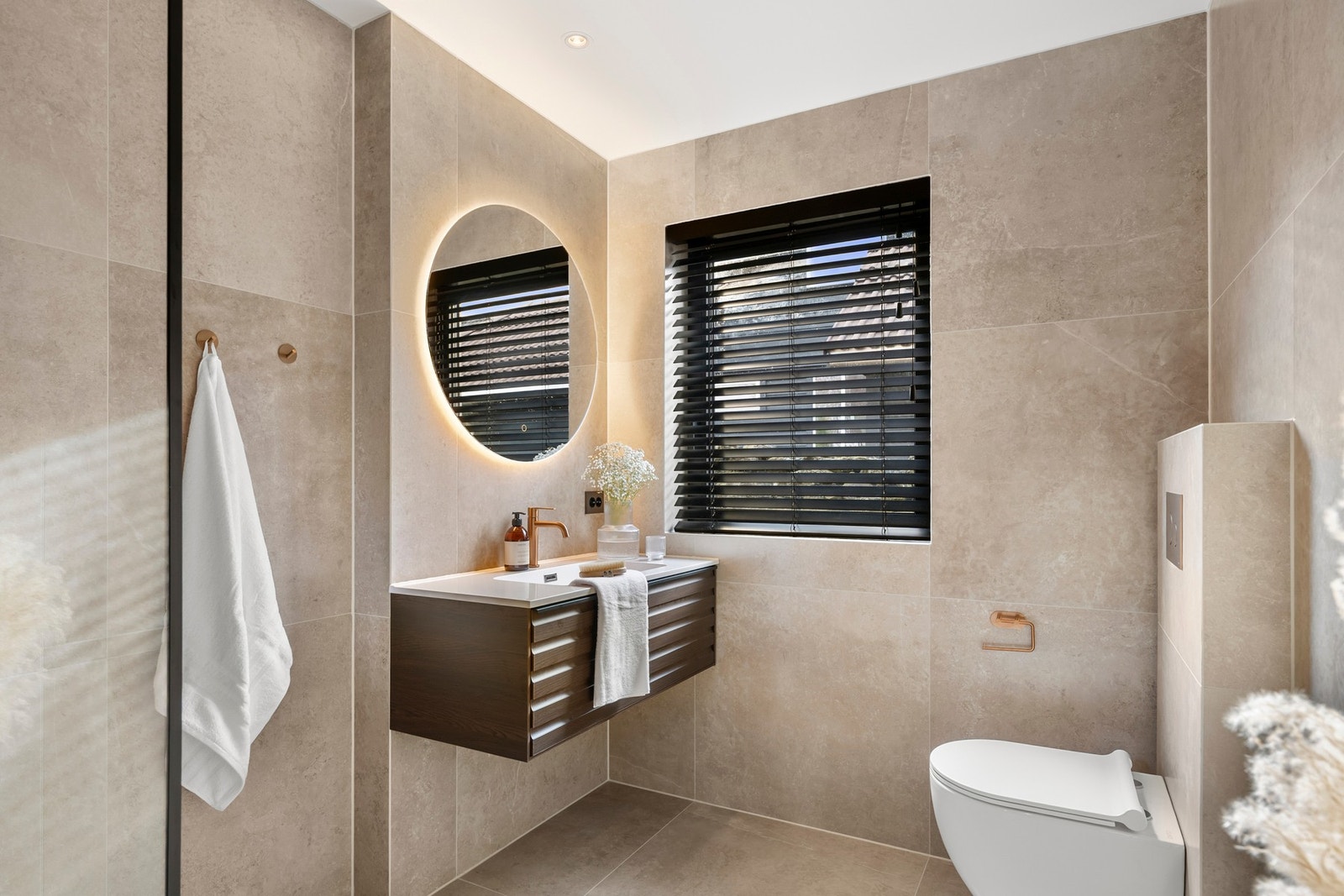 Baderomsinnredningen er moderne, med vegghengt servant med praktisk oppbevaringsskuff og rundt speil med integrert belysning. Galleribilde