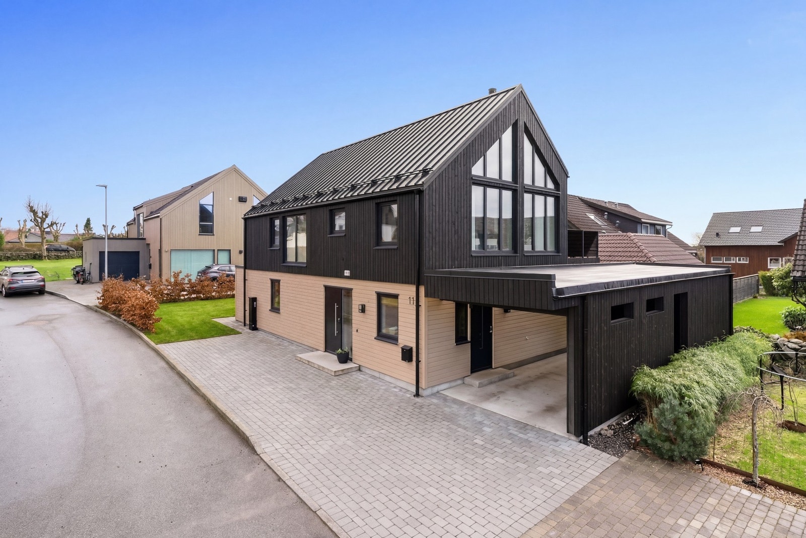 Boligen har en praktisk carport med installert elbillader, videre har man et stort gårdsrom med plass til ytterligere parkering (gressplen og gårdsrom er illustrert). Det er også blitt bygget en romslig utebod i enden av carporten med god plass til lagrin Galleribilde